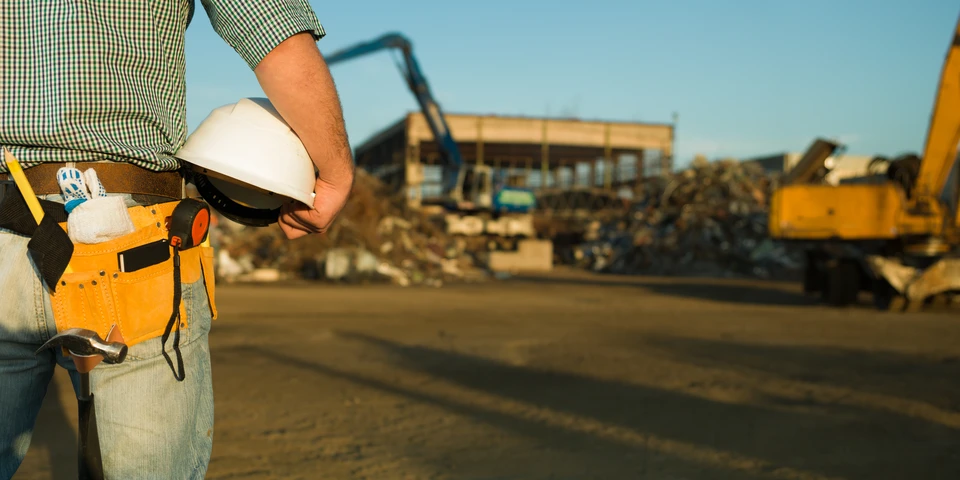 Chantier de construction en extérieur avec ouvrier du bâtiment portant ceinture à outils orange, casque de sécurité blanc et chemise à carreaux