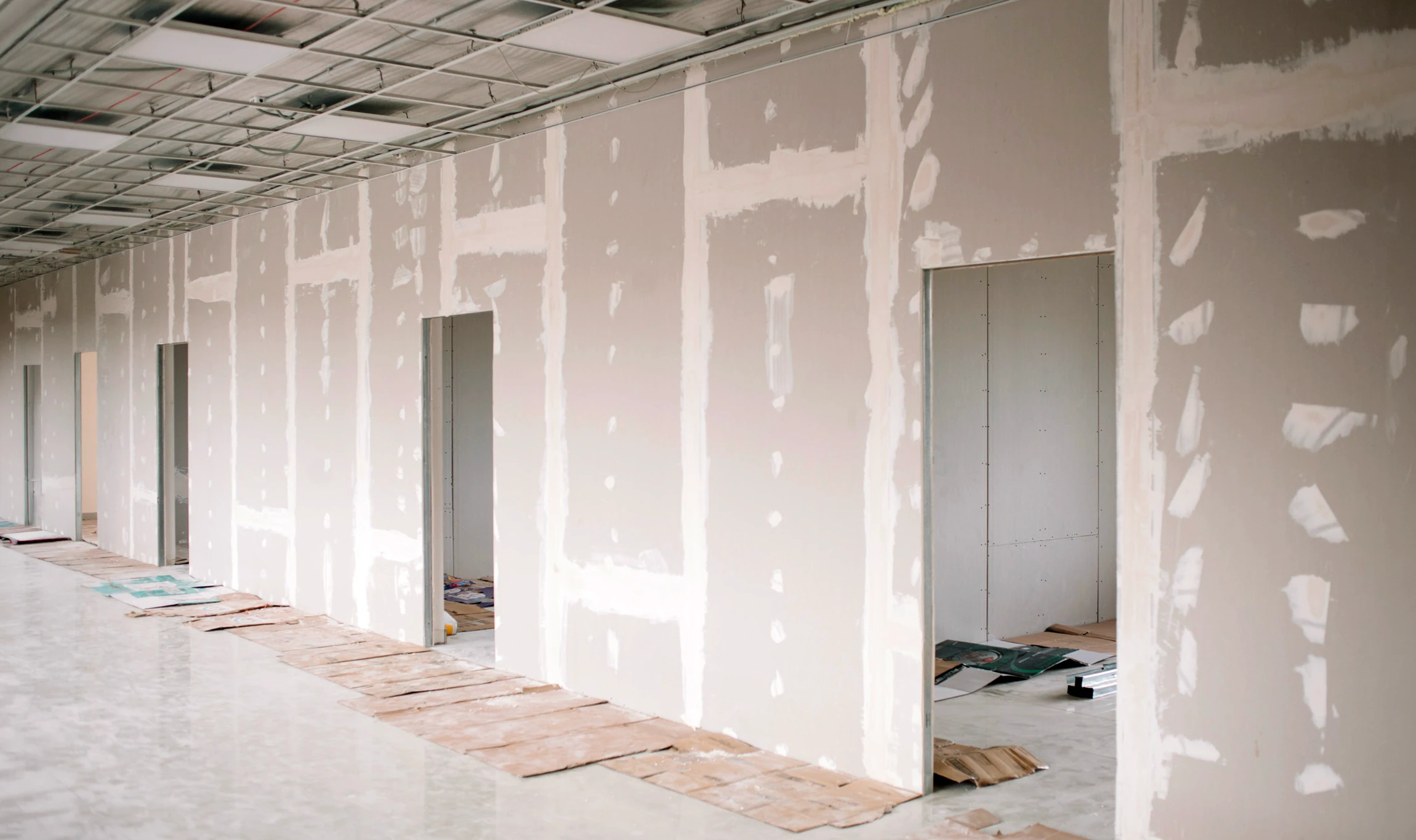 Ouvrier en tenue blanche utilisant une perceuse électrique sur un mur intérieur