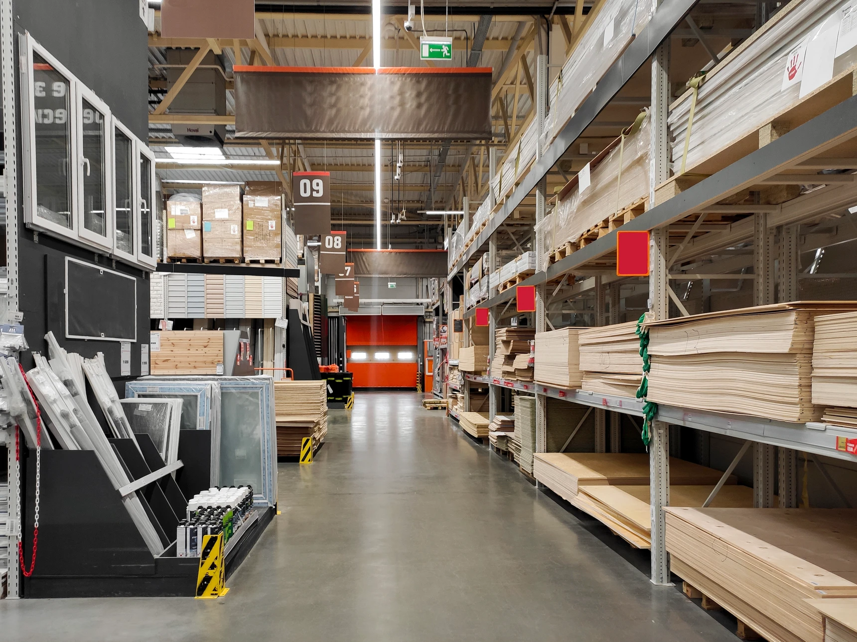 Entrepôt logistique moderne avec allées centrales, rayonnages métalliques bleus et orange à plusieurs niveaux